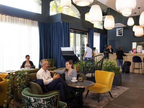 a man and woman sitting on couches in a lobby at Aparthotel Adagio Lyon Patio Confluence in Lyon