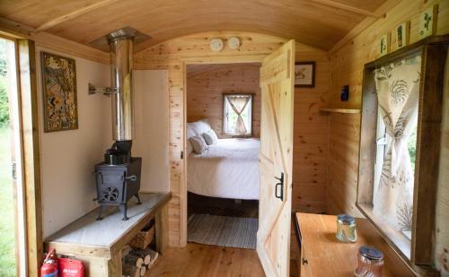 a tiny house with a bed and a wood stove at Honeysuckle Shepherds Hut at Blean Bees Eco Glamping in Canterbury