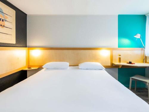 a bedroom with a large white bed and a chair at greet hôtel Angoulême in Saint-Yrieix-sur-Charente