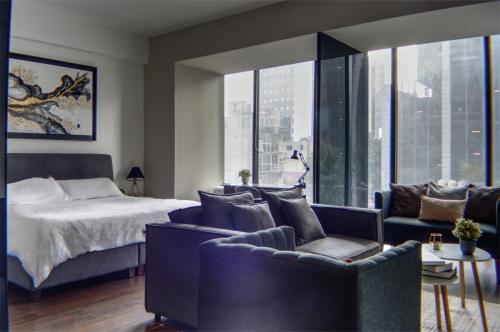 a bedroom with a bed and two chairs and a bed and windows at Reforma 284 King Size SUITE Swimming Pool, Parking & Kitchen in Mexico City