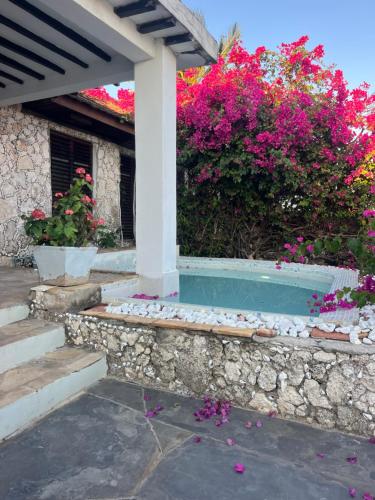 Una casa con flores rosas y un muro de piedra. en Malcom Ocean View Retreat, en Pongwe