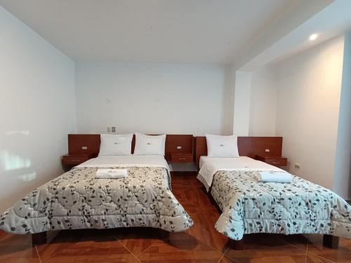 two beds in a room with white walls and wood floors at Misky Puñuy in Chiclayo