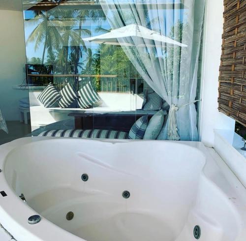 Una bañera blanca en una habitación con ventana. en Casa Ibiza Arraial d'Ajuda, en Arraial d'Ajuda