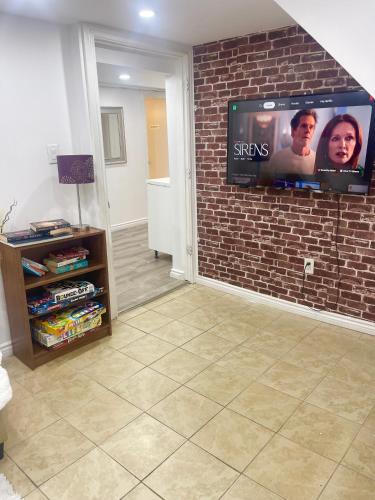 a living room with a tv on a brick wall at Modern & Cozy Basement Suite Lower Unit - 3 rooms -1 King bed - 2 Car Parking in Pickering