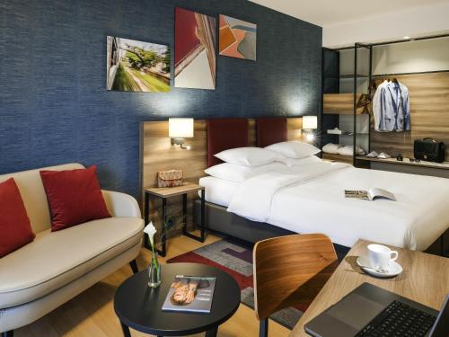 a hotel room with two beds and a couch and a desk at Mercure Geneva Airport in Geneva