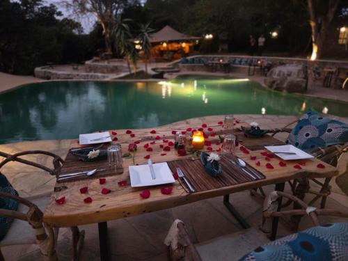 une table avec des bougies et des roses à côté d'une piscine dans l'établissement Dolly Farm & River Camp, Luxury Tents, à Usa River