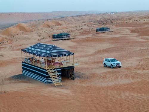 a car in the desert with a building in the sand at Desert Vibes Camp in Bidiyah