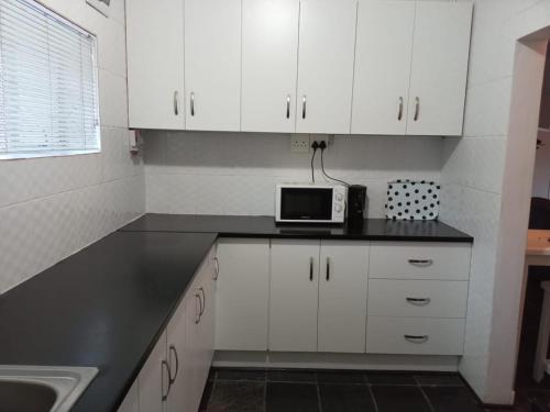 a kitchen with white cabinets and a microwave on a counter at Village on sea in Amanzimtoti