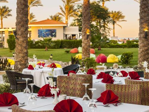 um restaurante com mesas brancas, guardanapos vermelhos e palmeiras em Rixos Sharm El Sheikh - Adults Only 18 Plus em Sharm El Sheikk