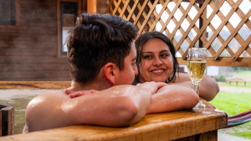 富特罗诺Turismo Jaos Cabañas Tinas y Quincho的一名妇女和一名男孩在热水浴缸中喝着一杯葡萄酒