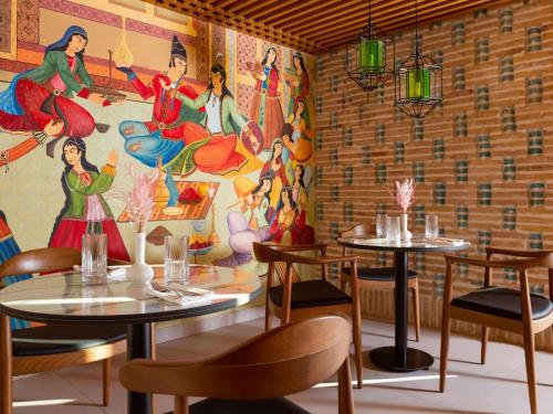 a restaurant with tables and chairs and a mural at Mercure Bukhara Old Town in Bukhara