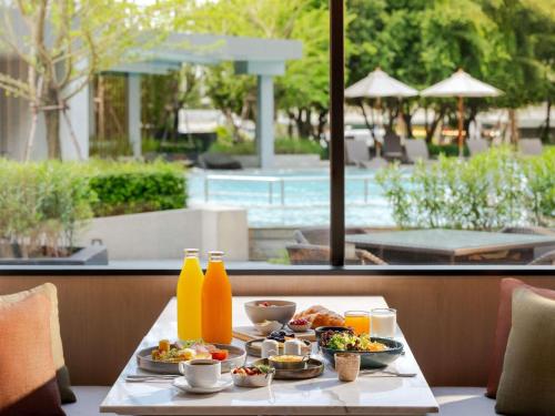 Una mesa con comida y bebidas con vista a una piscina. en Novotel Rayong Star Convention Centre, en Rayong