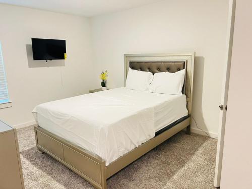 a bedroom with a bed with white sheets and a tv at The Evergreen Escape in Rosenberg