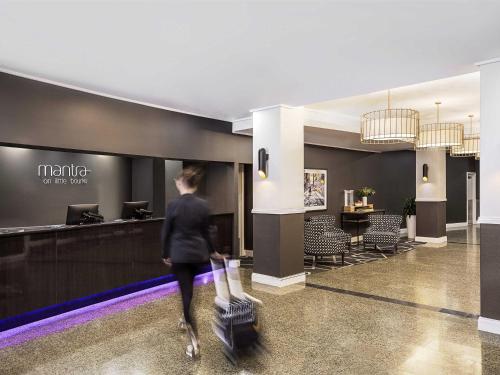 a woman walking through a lobby with luggage at Mantra on Little Bourke Melbourne in Melbourne