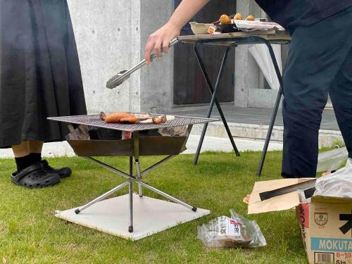 a man is cooking hot dogs on a grill at 一棟貸切鳥取の深緑に潜むモダン建築焙煎したての珈琲と休息を in Tottori