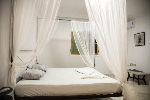 a bed with white curtains in a bedroom at La Villa 91 in Monastir