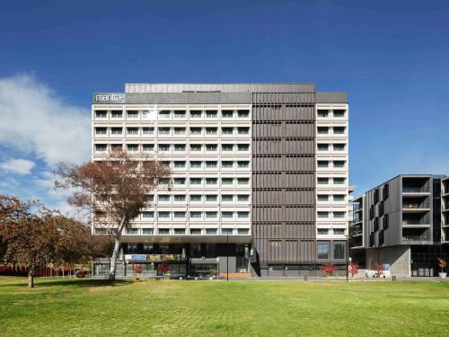 a large building with a grass field in front of it at Mantra MacArthur Hotel in Canberra