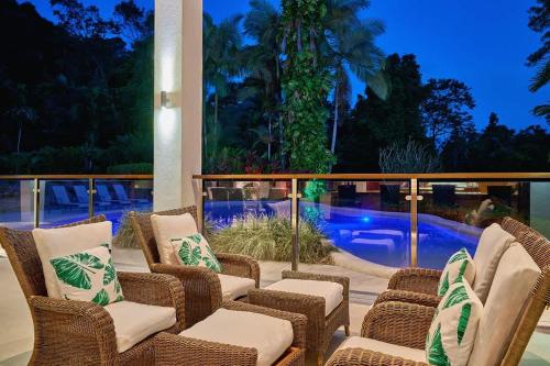a patio with wicker chairs and a pool at night at Ulysses Rainforest Retreat in Mossman
