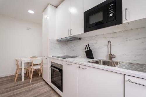 a white kitchen with a sink and a microwave at DesKanzo Guest House - Silva Brinco in São Mamede de Infesta