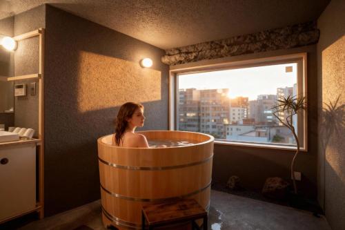 een vrouw zittend in een houten badkuip in een badkamer met een raam bij Mi-Kan Design Hotel in Tokyo