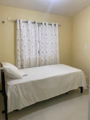 a bed in a room with a window with white curtains at Urban charm in Santo Domingo