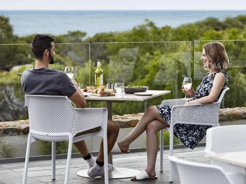 a man and woman sitting at a table with wine glasses at Pullman Bunker Bay Resort Margaret River in Dunsborough