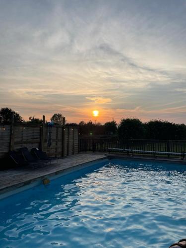 a swimming pool with the sunset in the background at Alfie Acres - Secluded Cabin set in 5 Acres of Privacy, with Exclusive use of Swimming Pool and Hot Tub for up to 10 Guests in Downham