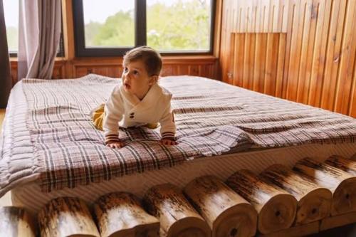 a baby laying on a bed next to a pile of logs at Niko Mamasakhlisi Guest House in Ozurgetʼi