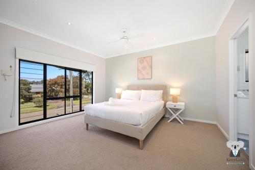 a white bedroom with a bed and a large window at KozyGuru | Chittaway Point | Lakeside Luxe Retreat in Chittaway Point