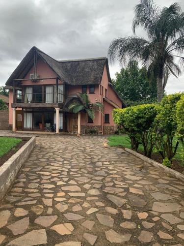 a house with a palm tree and a stone driveway at Ezulwini Thatch in Ezulwini