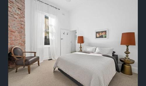 a white bedroom with a bed and a chair at Donatella, Where Heritage Meets Haute Living in Bendigo