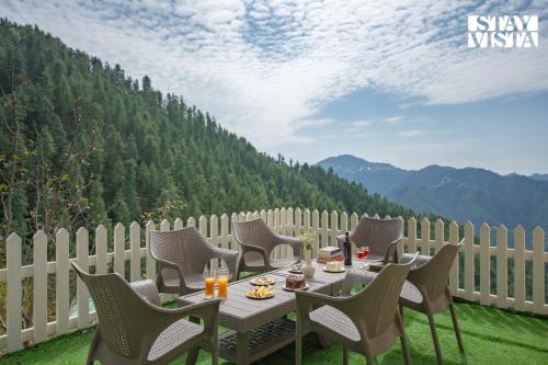 a table and chairs on a patio with mountains in the background at StayVista at Ved Vilas in Kīar