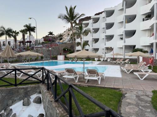 a swimming pool with chairs and a building at Apartamento Victoria in Mogán