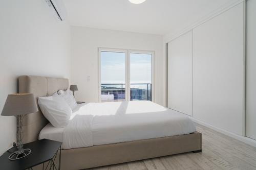 a white bedroom with a large bed and a window at Villa Zen with sea view and private pool in Lourinhã