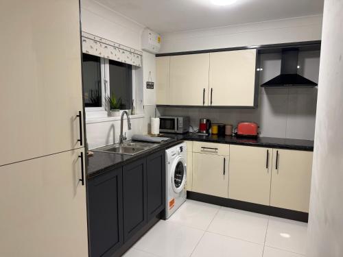 a kitchen with white cabinets and a sink and a dishwasher at Ibate Apartment, Basildon Essex in Nevendon