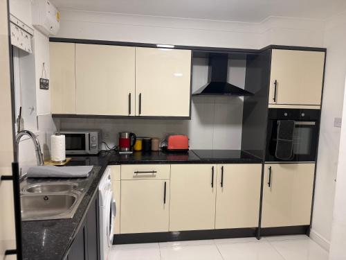 a kitchen with white cabinets and black counter tops at Ibate Apartment, Basildon Essex in Nevendon