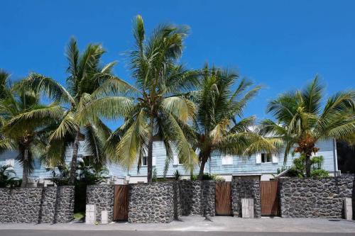 une maison blanche avec des palmiers derrière une clôture dans l'établissement COTTAGE OCEAN classé 3 étoiles - 4 à 6 personnes - 2 chb - Accès direct à la plage et à l'esplanade de Boucan Canot avec ses bars et restaurants, à Saint-Gilles les Bains