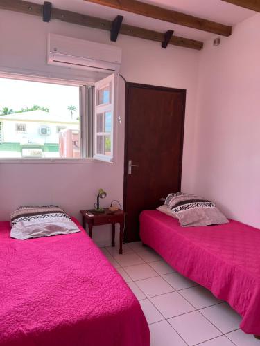 2 camas en una habitación con sábanas rosas y ventana en Haut de villa Espérenza, en Les Abymes