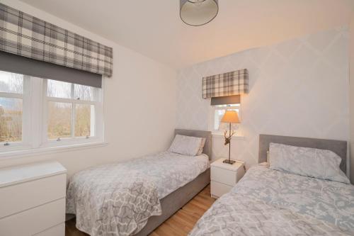 two beds in a bedroom with two windows at The Lodge House Callander in Callander