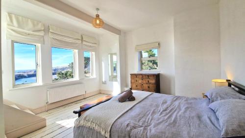 Un dormitorio con ventanas y una cama con un gato encima. en Main House at White Horses, Bantham, South Devon with panoramic sea views across to Burgh Island, en Bantham