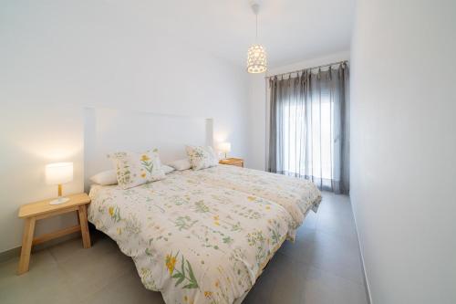 a white bedroom with a bed and a table with a lamp at Ático con gran terraza privada cerca de la playa in Nerja