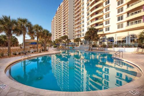 a large swimming pool with palm trees and buildings at Wyndham Ocean Walk Resort 2BR Apartment with Resort Access in Seabreeze