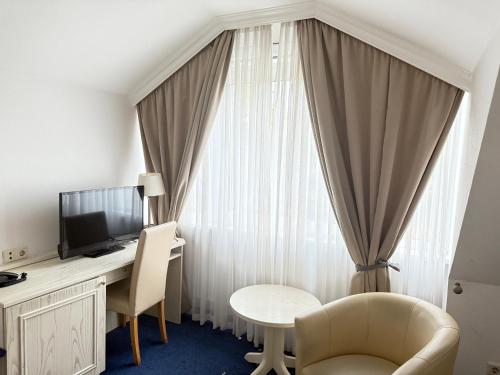 a room with a desk with a television and a table at HOTEL S Norderstedt in Norderstedt