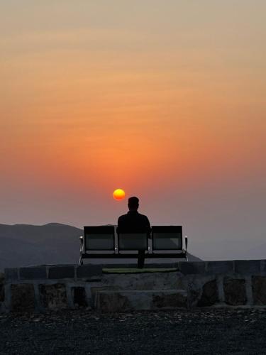 a man sitting on a bench watching the sunset at Jabal Shams, the summit house in Misfāh
