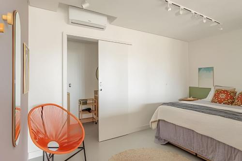 a white bedroom with a bed and a chair at Loft Moderno, 500m Praia, Piscina, Sauna, WiFi 1GB in Florianópolis