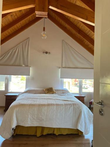 a bedroom with a bed with white sheets and windows at Cabaña Macar in Caviahue