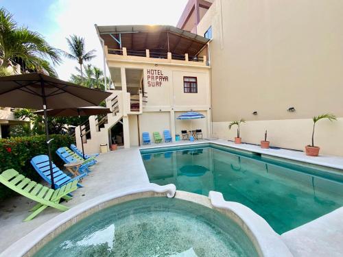 a swimming pool with chairs and an umbrella next to a building at Hotel Papaya Surf in Puerto Escondido
