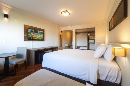 a hotel room with a large bed and a desk at Suíte Confort - Resort no Coração de Gramado in Gramado