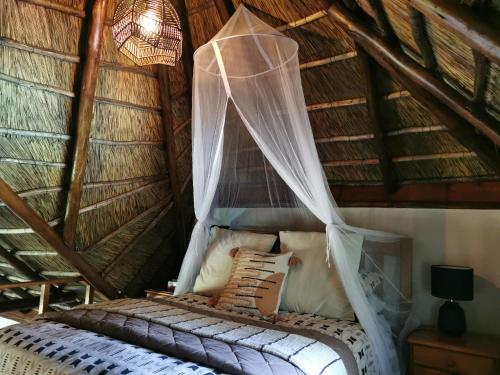 a bed in a thatched room with a mosquito net at The Thatched Cottage in Benoni