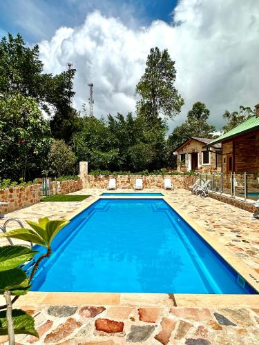 a blue swimming pool with two chairs and a house at Magnífica Cabaña en Pony Parque Mesa de los Santos in Piedecuesta